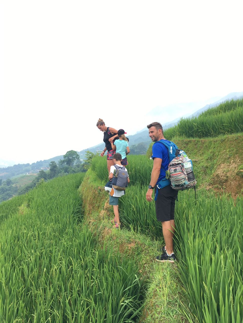 A group of people standing on a grassy hill with a mountainous background.