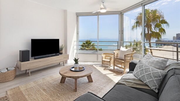 A modern living room with a large TV, comfortable seating, a wooden coffee table, and a balcony with a view of the sea. - Welgelegen 608 (Cape Town)