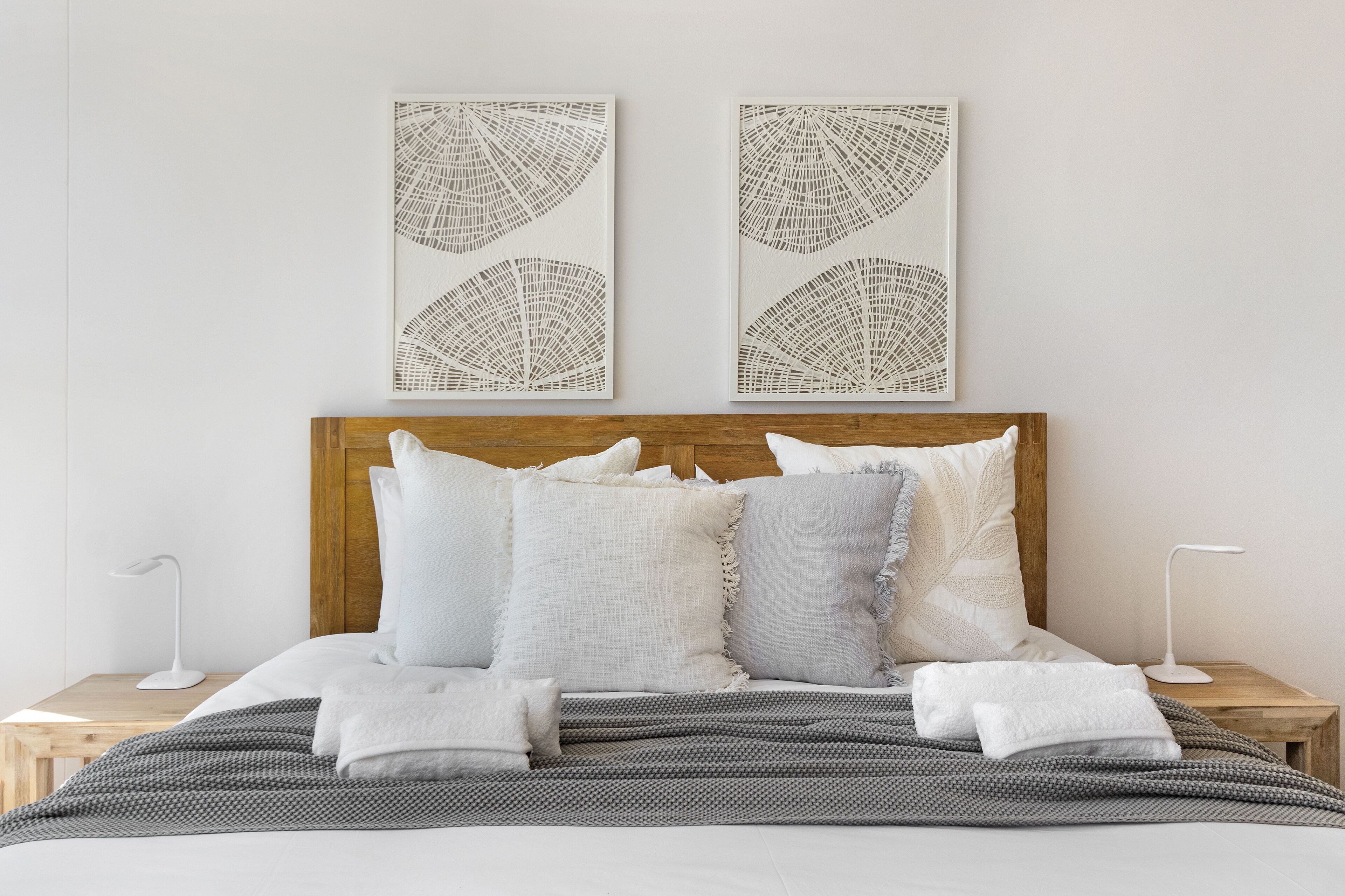 A neatly made bed with a wooden headboard, white and gray bedding, and two wall art pieces above it.