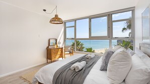 A bedroom with a large window, a bed with white linens, a wooden dresser, and a hanging light fixture. - Welgelegen 608 (Cape Town)
