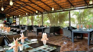 An indoor dining area with tables set for service, a wooden ceiling, and large windows allowing natural light.