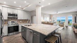 A modern kitchen with stainless steel appliances, a large island, and a view to the living area. - Summit at Tops`l 810 - Beautiful Gulf Views! (Miramar Beach)
