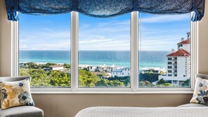 A bedroom with a large window overlooking a coastal view, including the ocean and nearby buildings. - Summit at Tops`l 810 - Beautiful Gulf Views! (Miramar Beach)