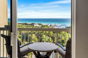 Un balcon avec vue sur l’océan et une maison blanche en arrière-plan.