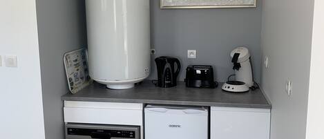 A compact kitchenette with a built-in dishwasher, a coffee maker, a kettle, and a toaster.