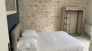 A bedroom with a stone wall, a bed with white bedding, a wardrobe, and a radiator. - PORT-DES-BARQUES (Port-des-Barques)