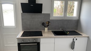 A modern kitchen with a built-in oven, a black range hood, a sink, and a window above the sink. - PORT-DES-BARQUES (Port-des-Barques)