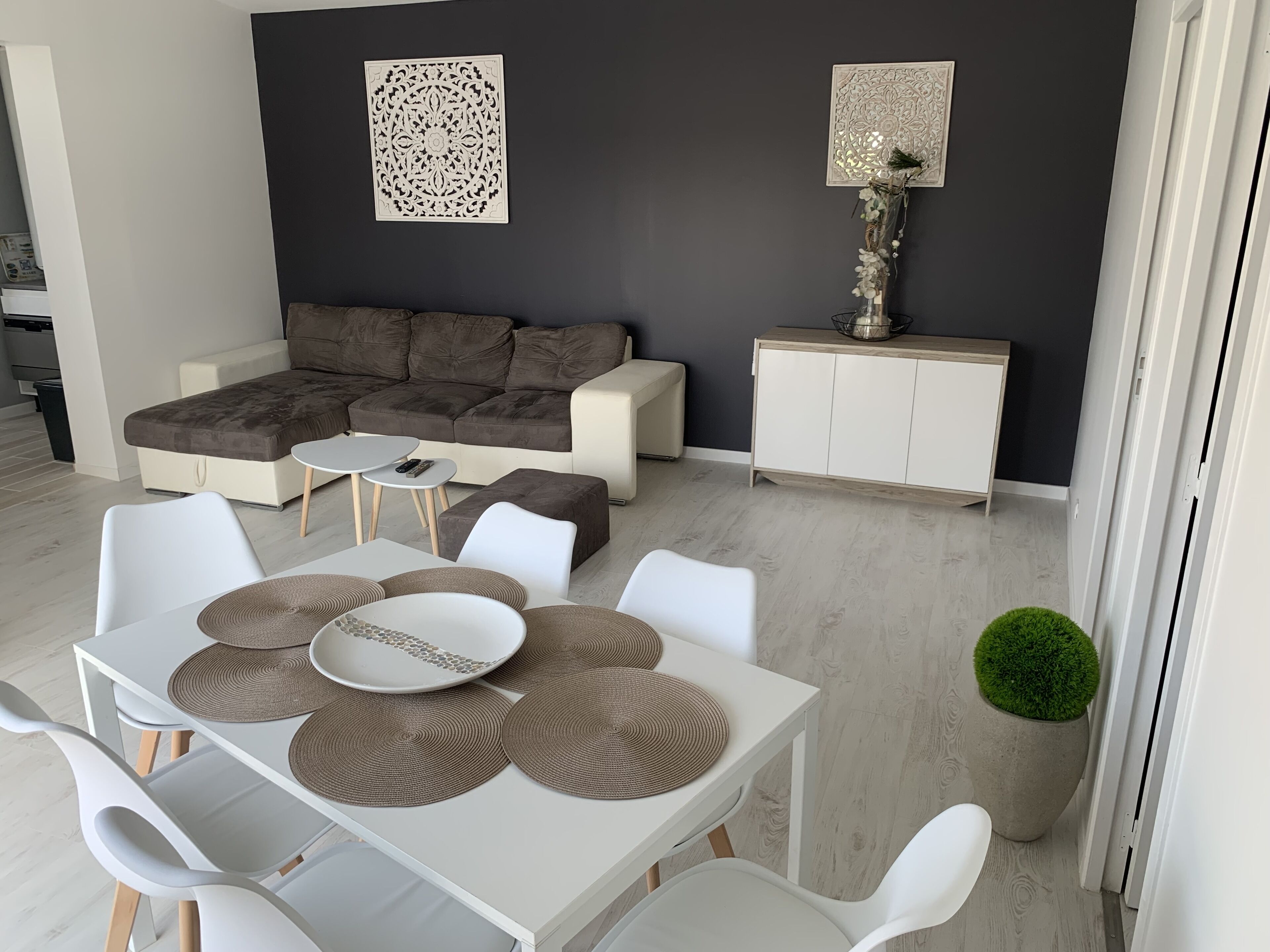 Uma sala de estar moderna com um sofá seccional, uma mesa de jantar com jogos americanos e arte decorativa na parede.
