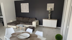 A modern living room with a sectional sofa, a dining table with placemats, and decorative wall art. - PORT-DES-BARQUES (Port-des-Barques)