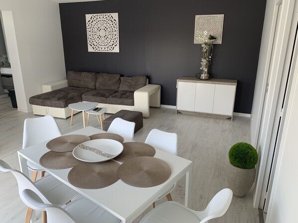 En moderne stue med en hjørnesofa, et spisebord med servietter og dekorativ vægkunst.