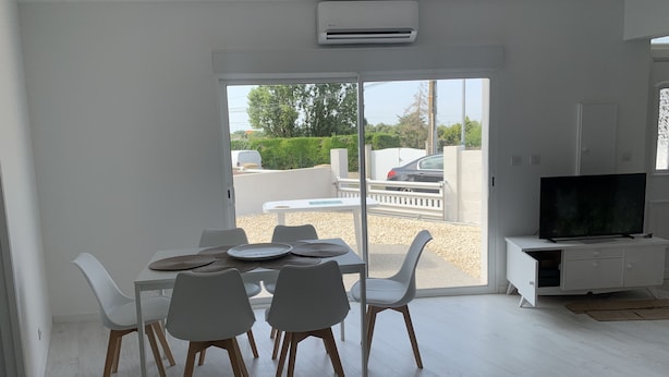 A modern living room with a dining area, a flat-screen TV, and a sliding glass door leading to an outdoor patio. - PORT-DES-BARQUES (Port-des-Barques)