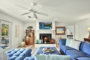 A living room with a fireplace, blue sofas, a ceiling fan, and a large painting.