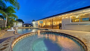 A swimming pool with a tiled edge, a covered patio area with outdoor furniture, and a house with large windows and a garage. - Open Labor Day Weekend |HTD Pool | 6 TVS | 2 King beds (Bradenton)