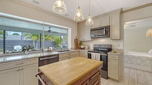 A modern kitchen with a large window, stainless steel appliances, and a wooden dining table. - Open Labor Day Weekend |HTD Pool | 6 TVS | 2 King beds (Bradenton)