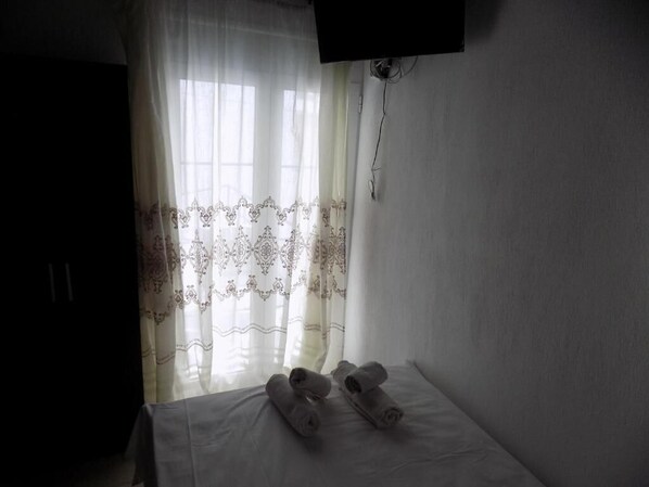 A room with a bed, a TV mounted on the wall, and a window with sheer curtains.