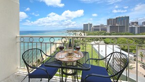 A balcony with a table, two chairs, and a view of the beach and cityscape.