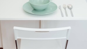 A white dining table with a teal bowl and spoon set, a white chair, and small potted plants on the table.