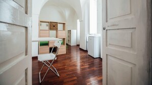 A spacious room with a wooden floor, a white desk, a chair, and a small white cabinet.