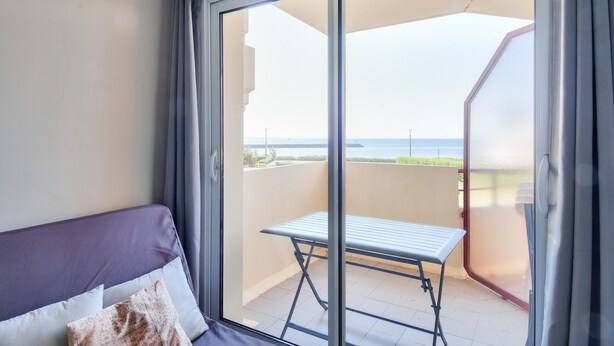 Un balcone con tavolo e sedie, un divano con cuscini e vista mare.
