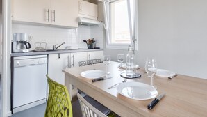 Una cucina moderna con mobili bianchi, lavastoviglie e zona pranzo apparecchiata con piatti, bicchieri e posate.