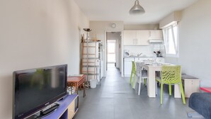 Una cucina moderna con mobili bianchi, un'area pranzo con tavolo e sedie e un televisore su un supporto.