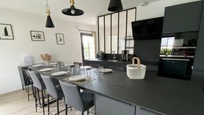 A modern kitchen with a central island, bar stools, and a large window providing natural light. - Surf & swimming – 300 m from Pors Carn beach (Penmarch)