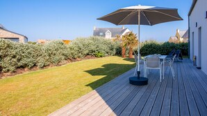 A wooden deck with a table and chairs, an umbrella, and a well-maintained lawn. - Surf & swimming – 300 m from Pors Carn beach (Penmarch)