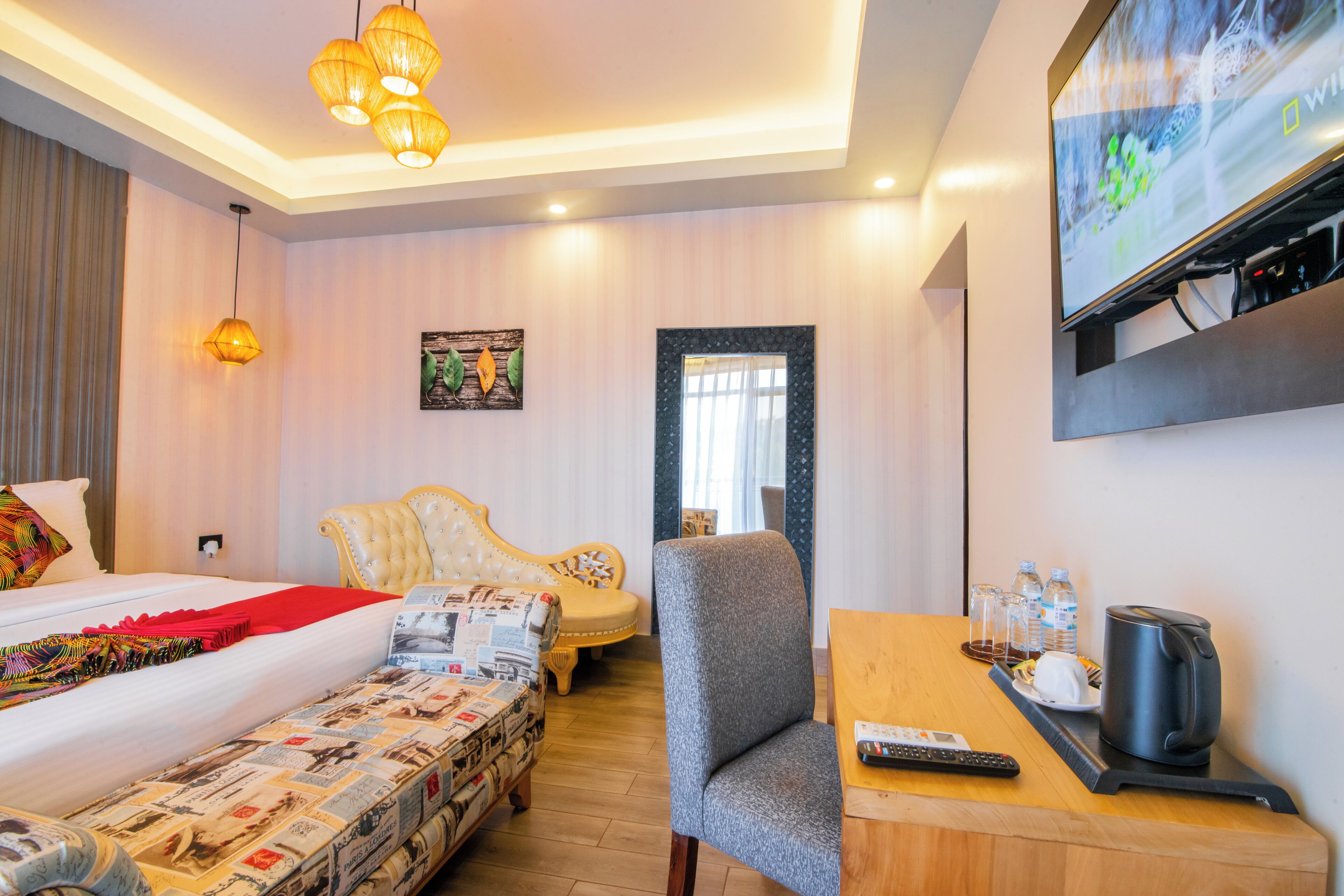 A hotel room with a bed, a sofa, a chair, a TV, a coffee maker, and a table with water bottles.
