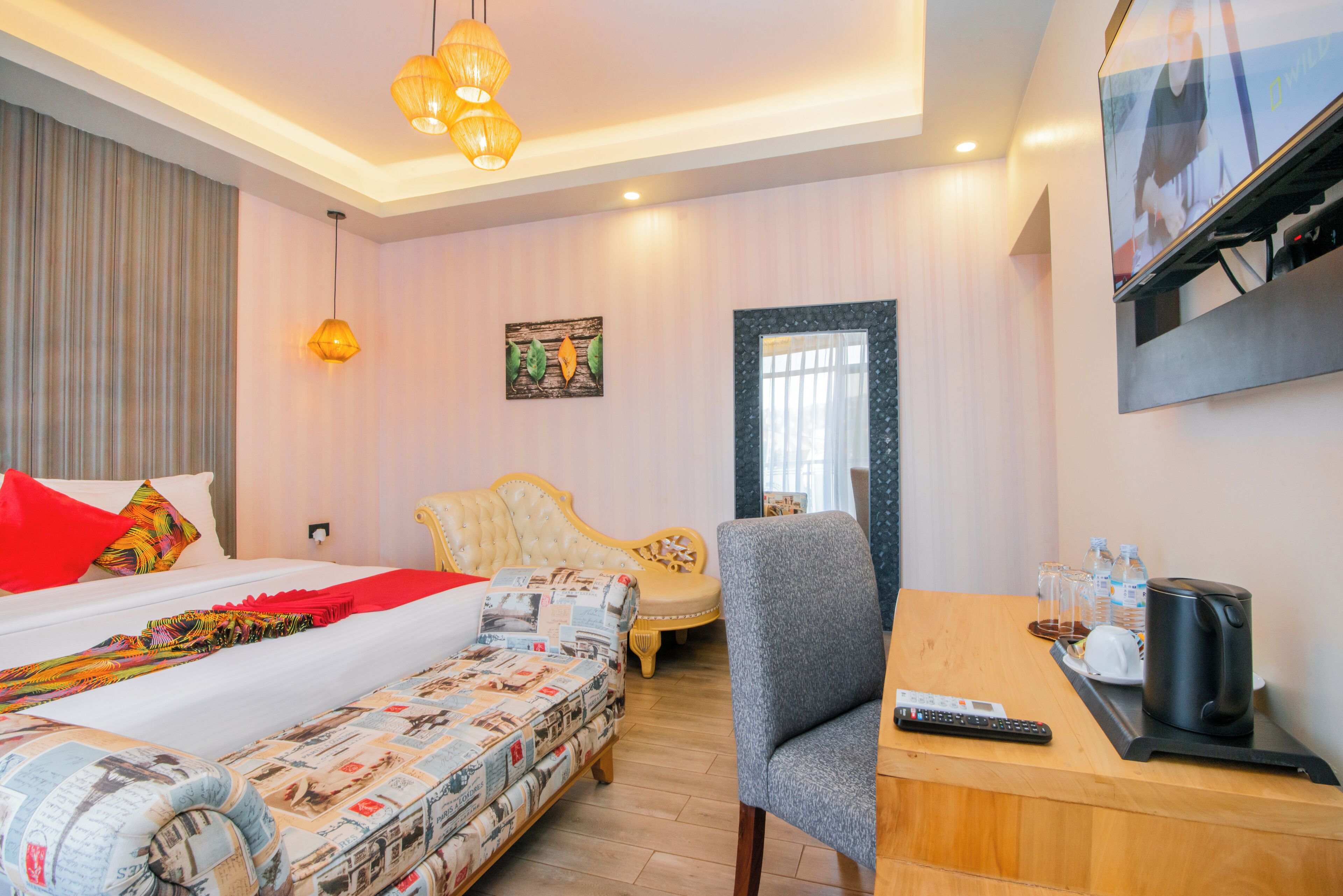 Quarto de hotel com uma cama, um sofá, uma cadeira, uma escrivaninha com chaleira e uma televisão.