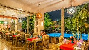Un restaurant avec des meubles en bois, des nappes rouges et une vue sur la piscine.
