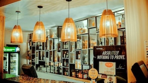 Un espace bar doté de plusieurs lampes suspendues, d’étagères remplies de bouteilles et d’un comptoir avec un terminal de paiement.