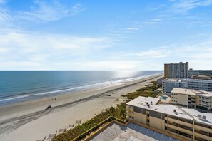 A beachfront hotel with a view of the ocean, a parking lot, and a building with multiple floors.