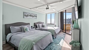 A bedroom with two beds, a ceiling fan, a large window, and a view of the city. - Completely Renovated Ocean View Unit + Free Attraction Tickets! (Myrtle Beach)
