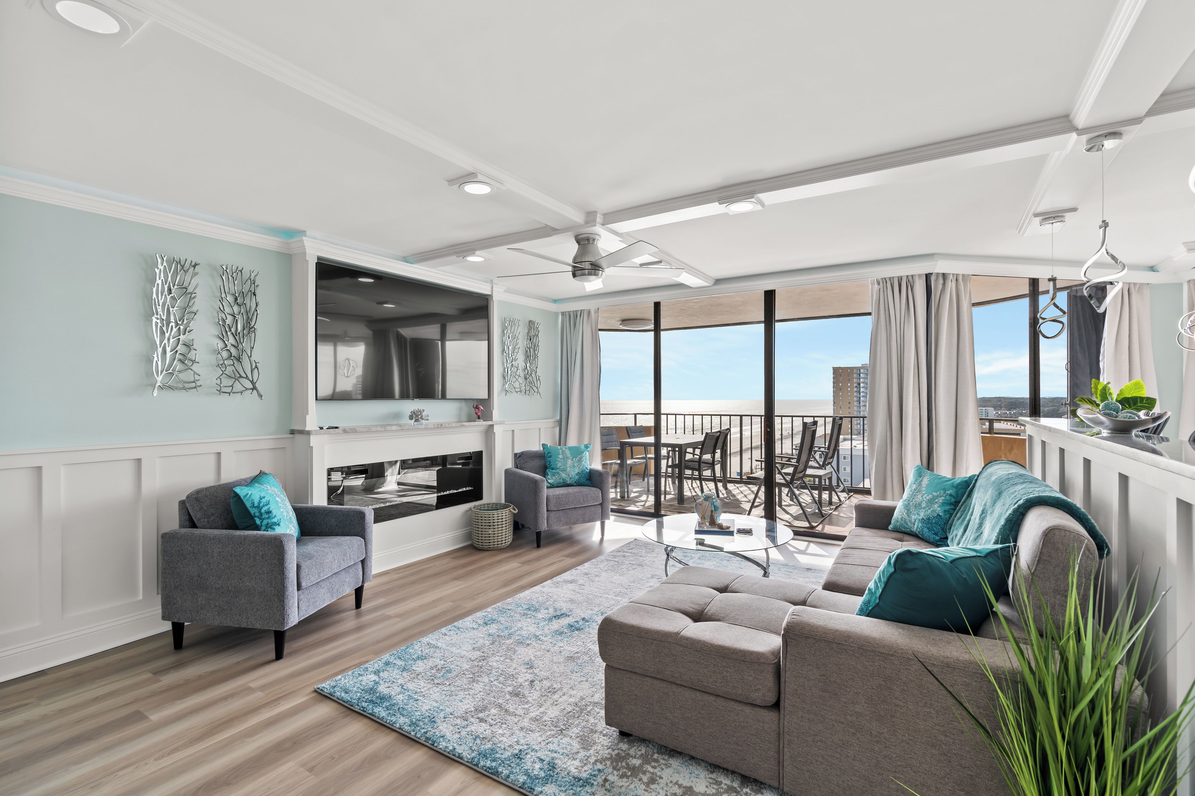 A spacious living room with a sofa, armchairs, and a coffee table. There is a balcony with a view of the city.