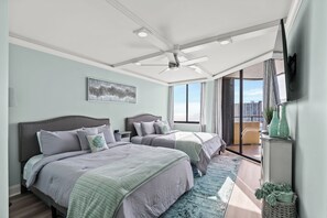 A bedroom with two beds, a ceiling fan, a large window, and a view of the city.