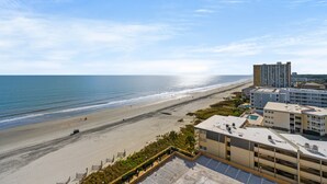 A beachfront hotel with a view of the ocean, a parking lot, and a building with multiple floors. - Completely Renovated Ocean View Unit + Free Attraction Tickets! (Myrtle Beach)