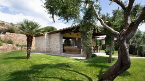 A stone house with a tiled roof, a patio with wicker furniture, and a well-maintained lawn.