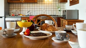 A breakfast setting with a wooden table, a fruit bowl, croissants, and a chocolate tart.