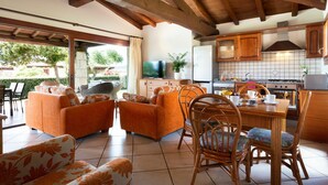 A spacious living area with a wooden ceiling, a dining table with chairs, and a kitchen area with cabinets and a refrigerator.