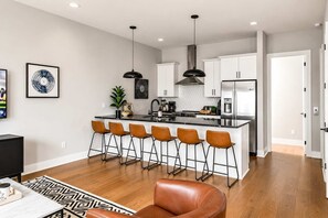 A modern kitchen with a central island, bar stools, and a dining area with a leather chair. - 2 Nashville Homes • Hot Tubs • Sleeps Up to 24 (Nashville)