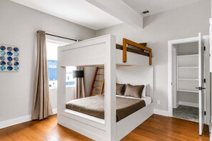 Una habitación con literas, una escalera, una puerta que da a un armario y una ventana con cortinas.