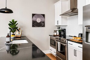 Une cuisine moderne avec un plan de travail noir, des appareils en acier inoxydable et une machine à café.