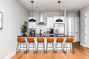 A modern kitchen with a central island, bar stools, and stainless steel appliances. - 2 Nashville Homes • Hot Tubs • Sleeps Up to 24 (Nashville)
