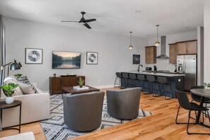 A modern apartment with a living room, dining area, kitchen, and a ceiling fan.