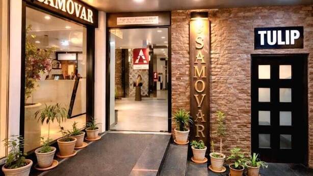 Entrada de un hotel con mostrador de recepción, plantas en macetas y señalización para los hoteles 'SAMOVAR' y 'TULIP'.
