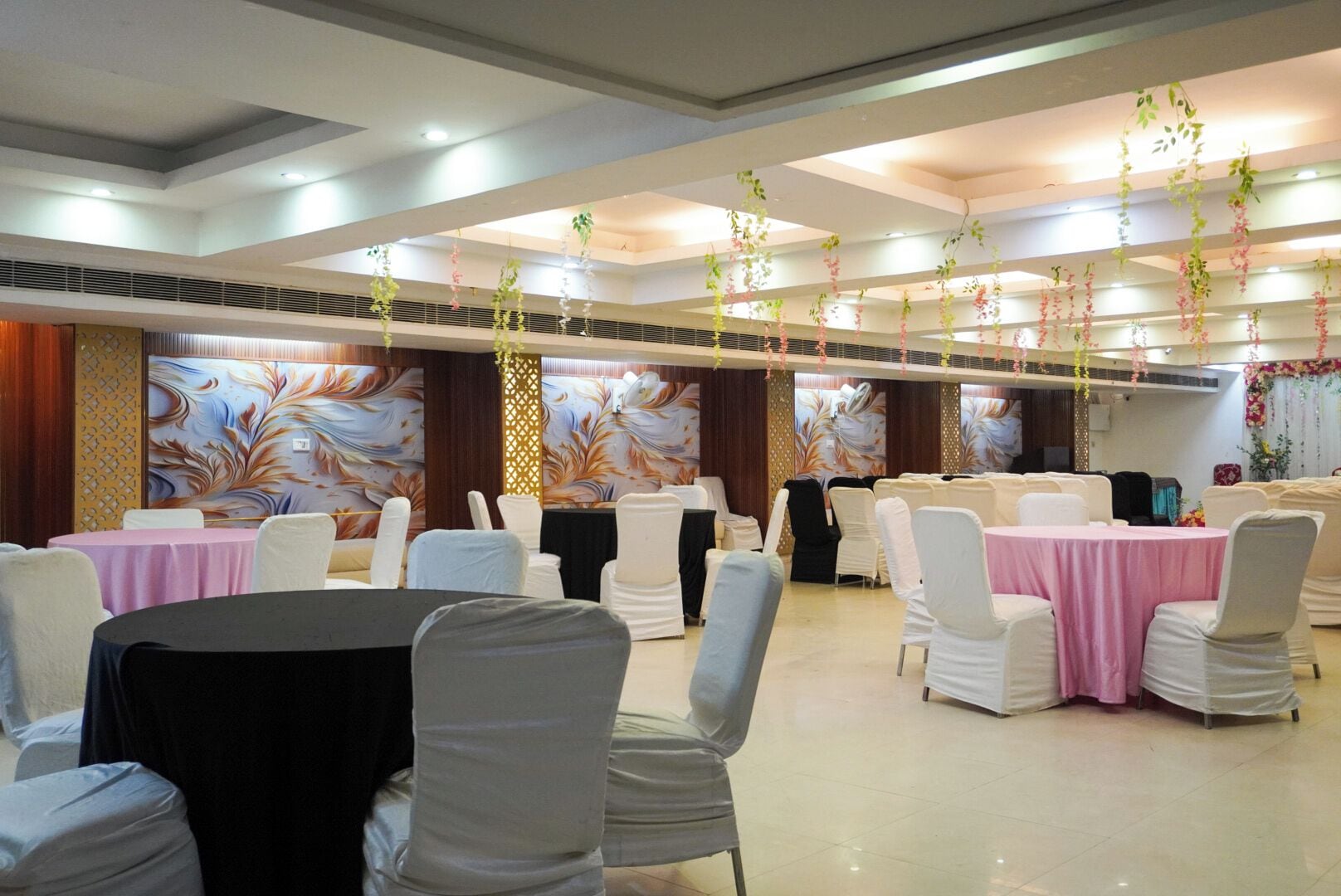 A banquet hall with round tables, white chairs, and floral decorations.