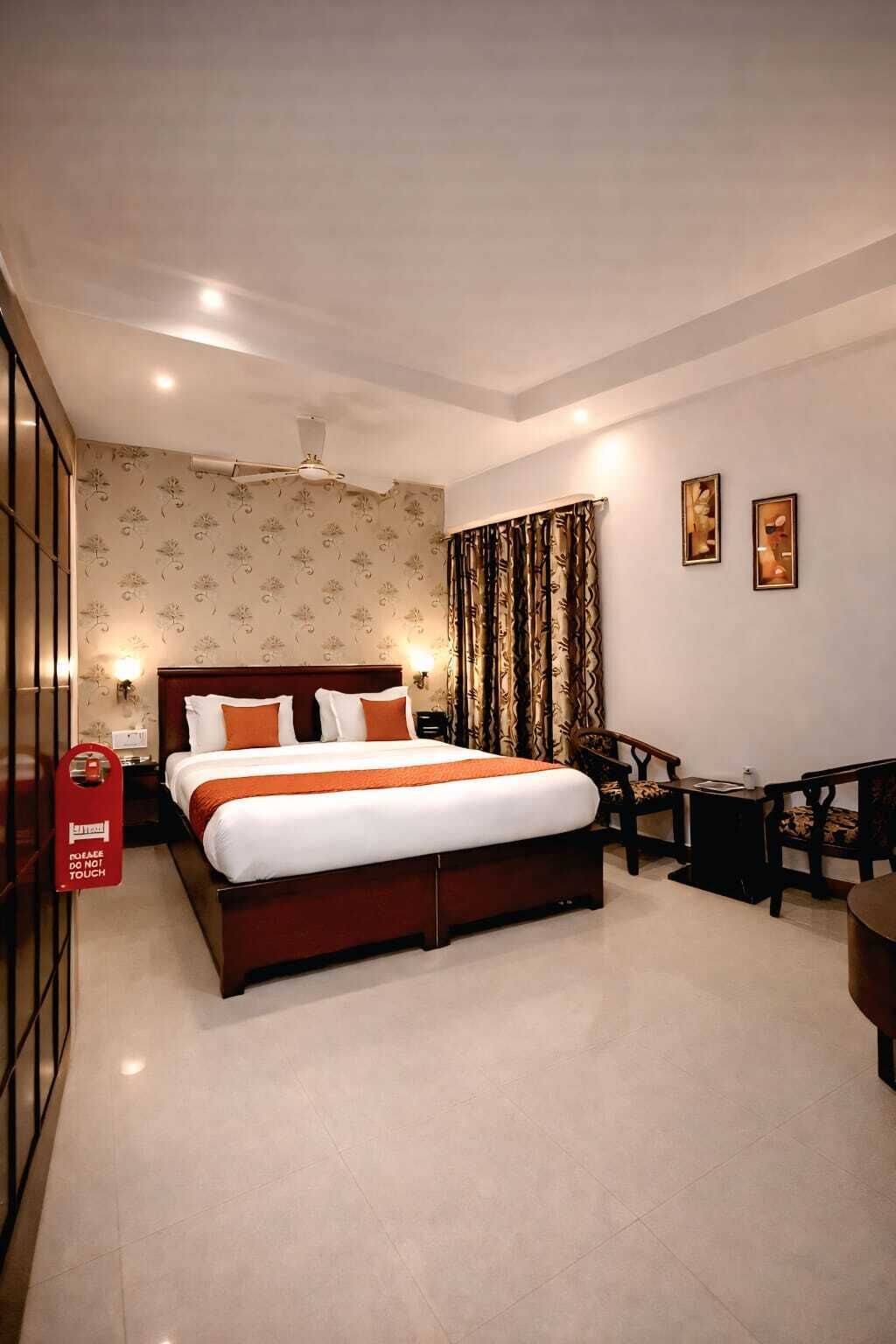 A hotel room with a bed, a desk, a chair, a ceiling fan, and a wall with two framed pictures.