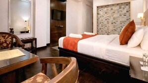 Habitación de hotel con cama, escritorio, silla, ventilador de techo y aire acondicionado.