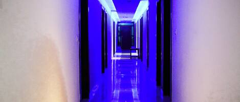 Een gang met een zwart-wit geruit vloertapijt en wanden verlicht met blauw licht.