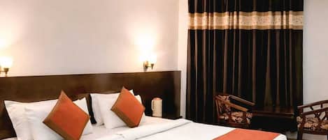 Ein Hotelzimmer mit einem großen Bett, einem Deckenventilator, einem Nachttisch, einem Sessel und einem Fenster mit Vorhängen.